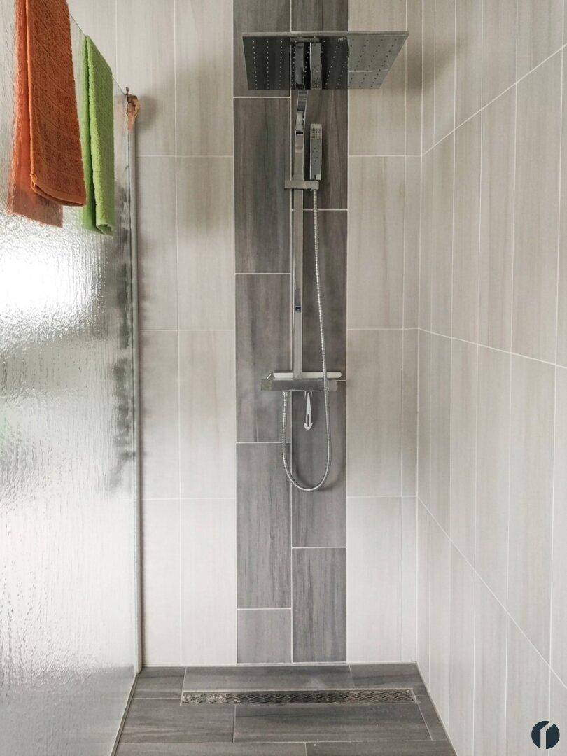 Moderne begehbare Dusche mit Regenduschkopf und grauen Fliesen im Badezimmer.