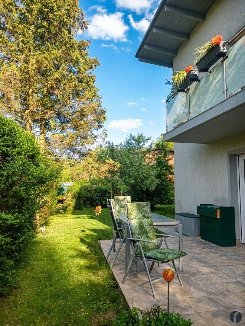 Sonniger Terrassenbereich mit Gartenmöbeln und Blick auf den grünen Garten und Balkon.