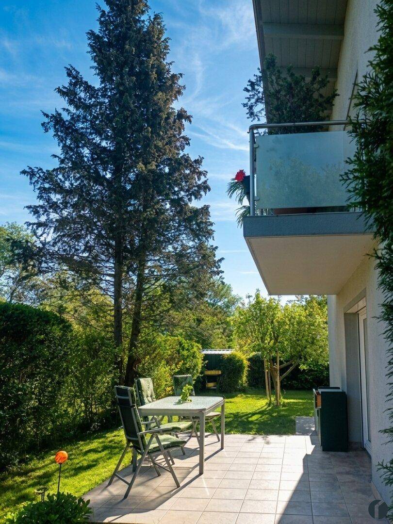 Gemütliche Terrasse mit Gartenmöbeln und weitem Blick auf den gepflegten Garten und hohe Bäume.