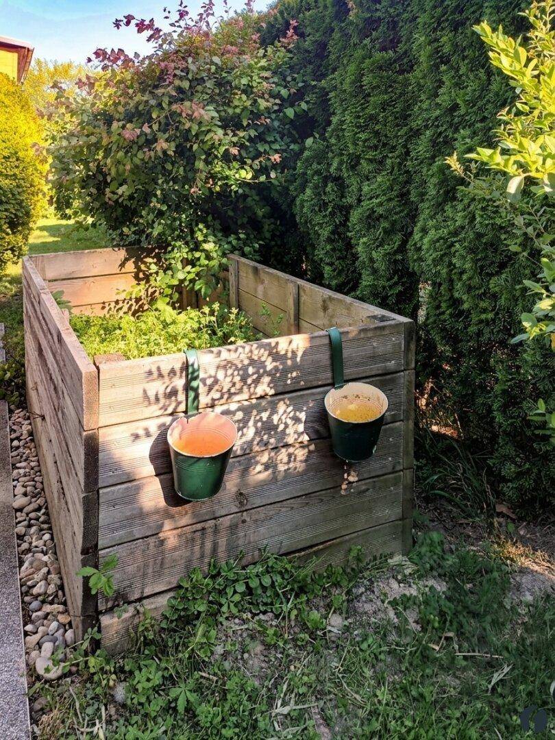 Hochbeet aus Holz im Garten, umgeben von grünen Hecken und Pflanzen.
