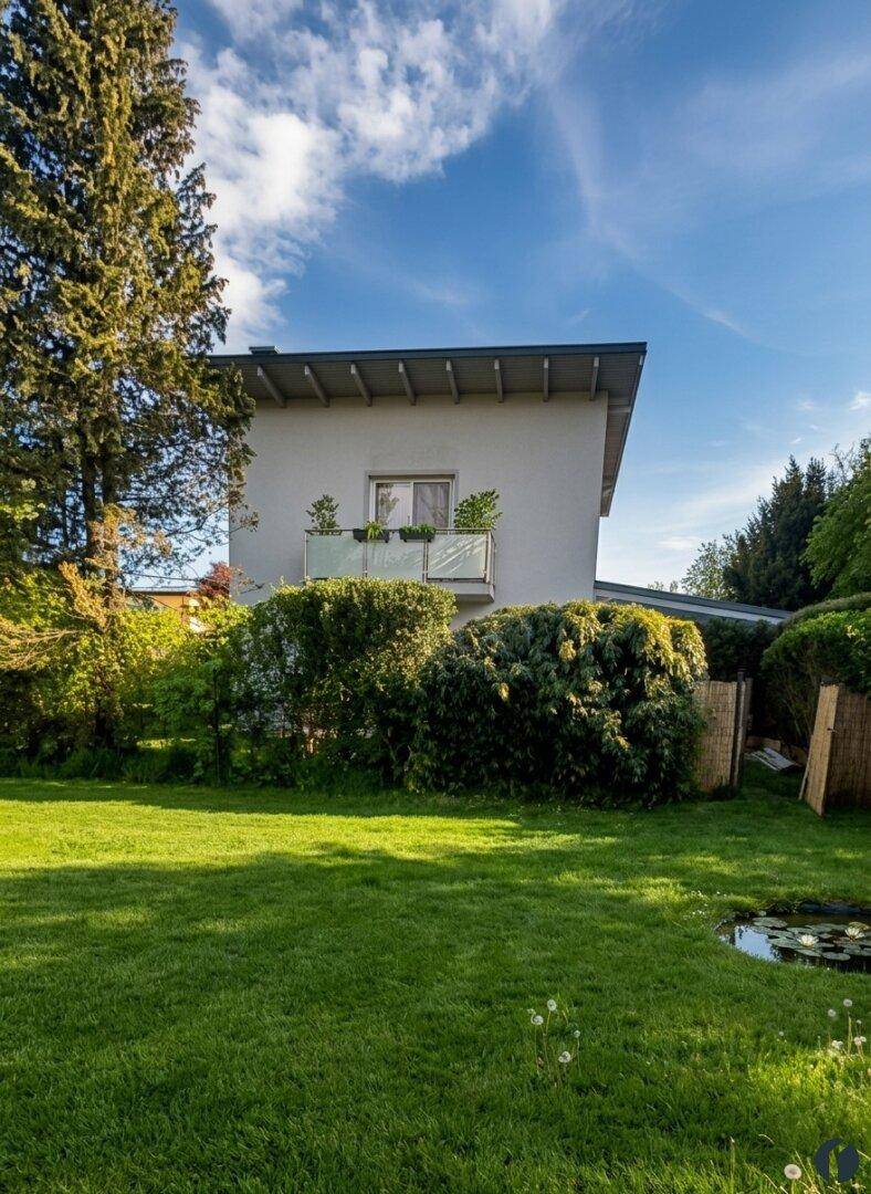 Gepflegter Garten mit Rasenfläche, kleinem Teich und Blick auf die Hausfassade mit Balkon.