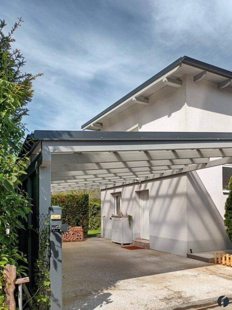 Überdachter Carport neben der Hausfassade mit Holzlager und gepflegter Einfahrt.