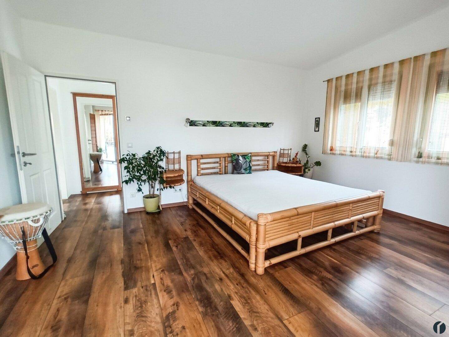 Helles Schlafzimmer mit Holzboden, Bambusbett und Zugang zu einem weiteren Raum.