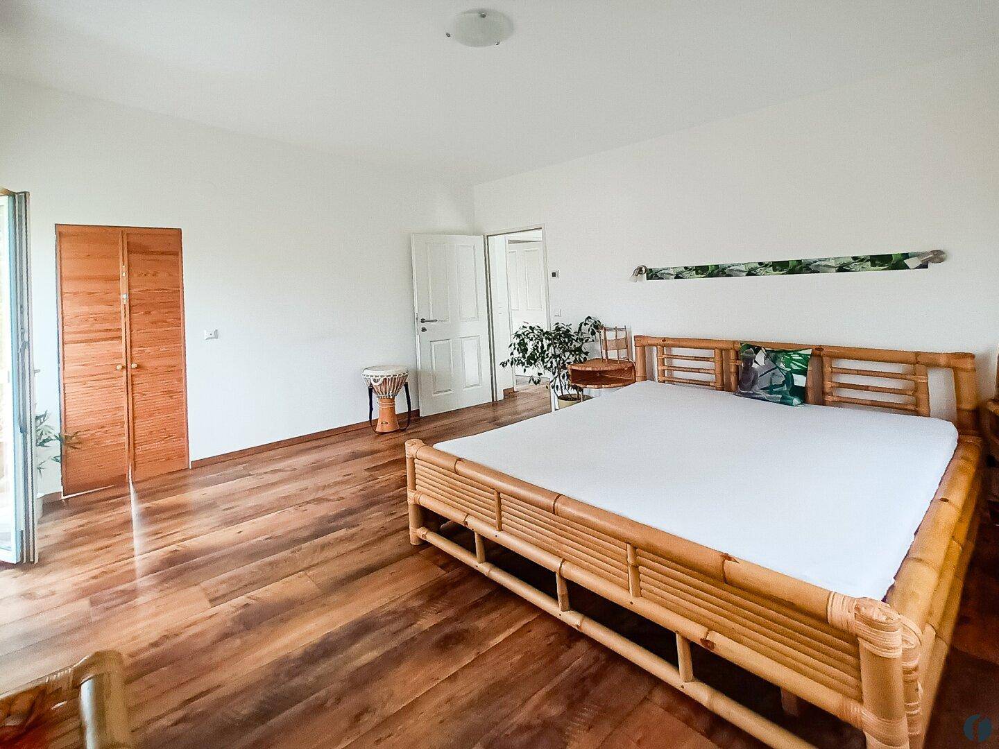 Geräumiges Schlafzimmer mit Holzboden und einem großen Bambusbett, hell und einladend.