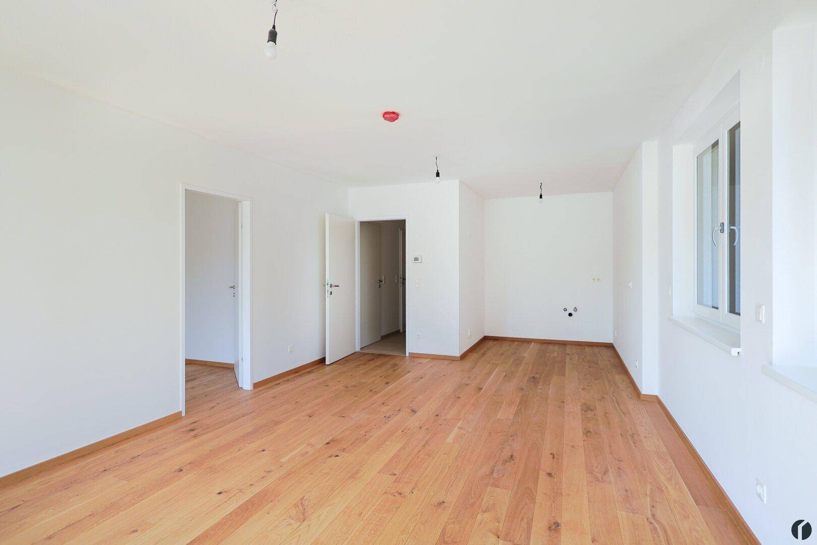 Heller, unmöblierter Raum mit Holzboden, vorbereitet für eine offene Küche und Essbereich.