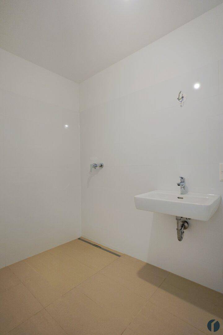 Unmöbliertes Badezimmer mit Fliesenboden und Anschlüssen für eine Dusche und Waschbecken.