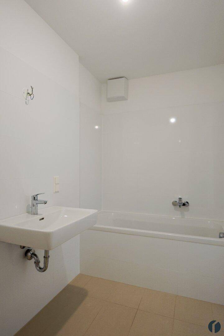 Unmöbliertes Badezimmer mit Badewanne, Waschbecken und hellen Fliesen.