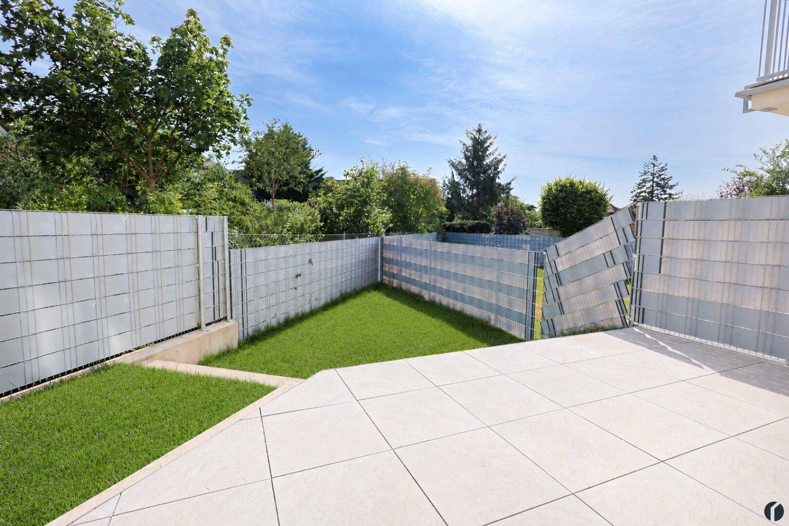 Sonniger Terrassenbereich mit angrenzendem Rasen und moderner Zaunanlage.