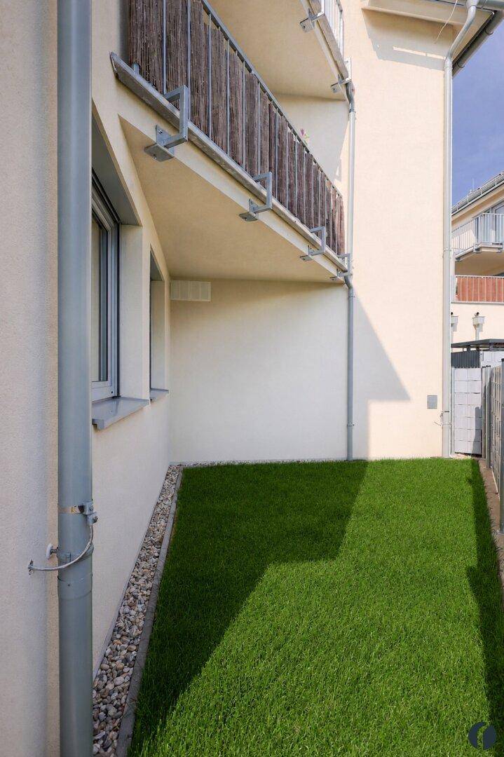 Seitenansicht des Gebäudes mit schmalem Rasenstreifen und Balkonen.