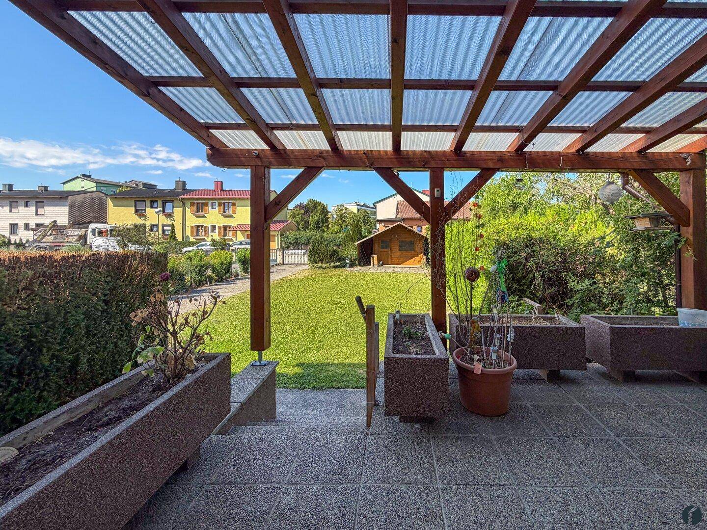 Überdachte Terrasse mit Holzbalken und Blick in den Garten mit Gartenhaus.
