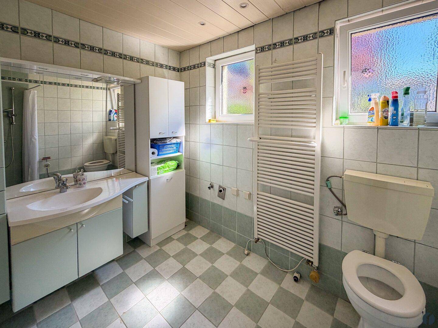Badezimmer mit hellblauen Fliesen, weißem Waschtisch, Fenster und beheiztem Handtuchhalter.