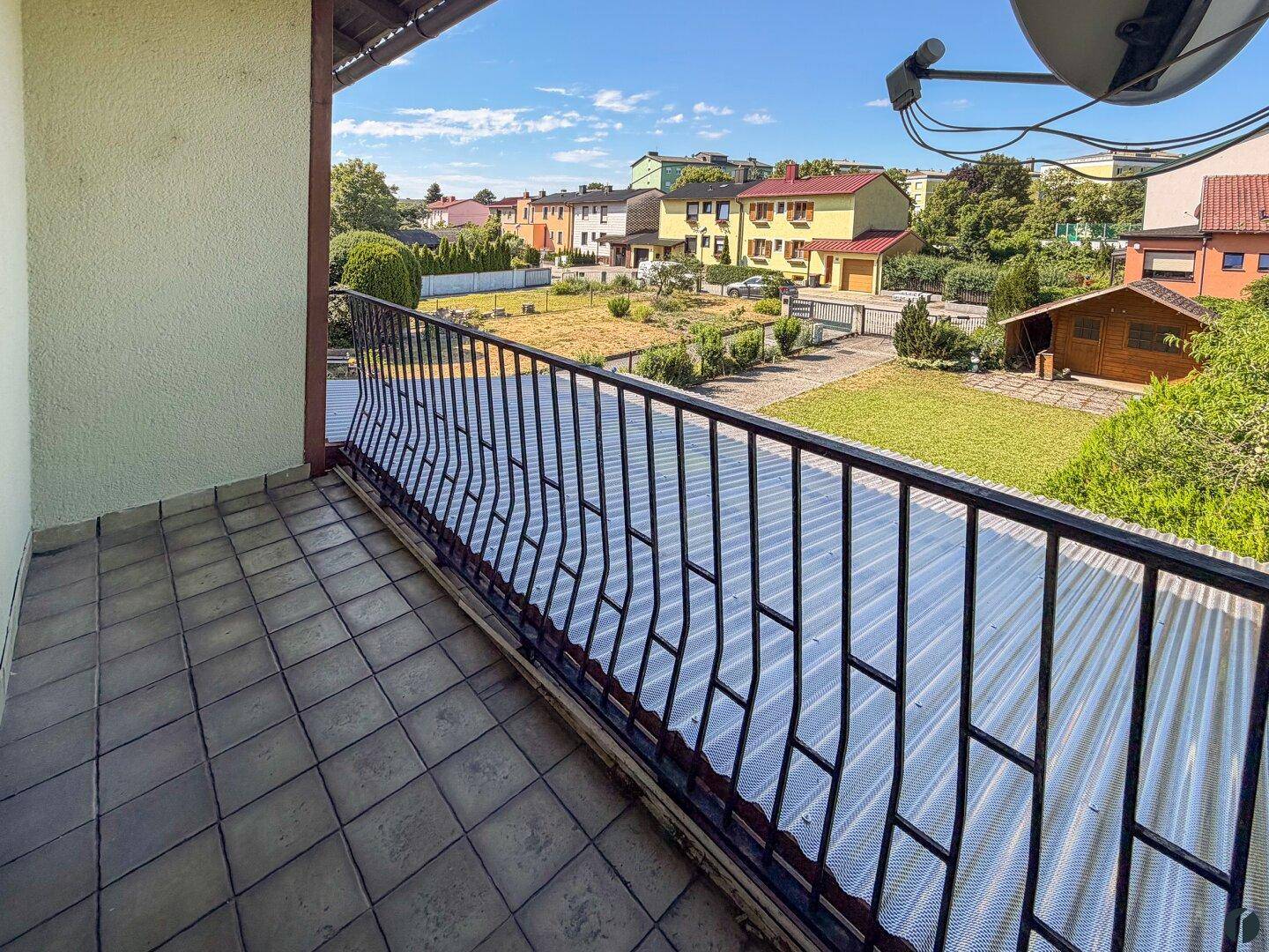 Balkon mit Fliesenboden und schmiedeeisernem Geländer, bietet Blick auf die Nachbarschaft und Gärten.