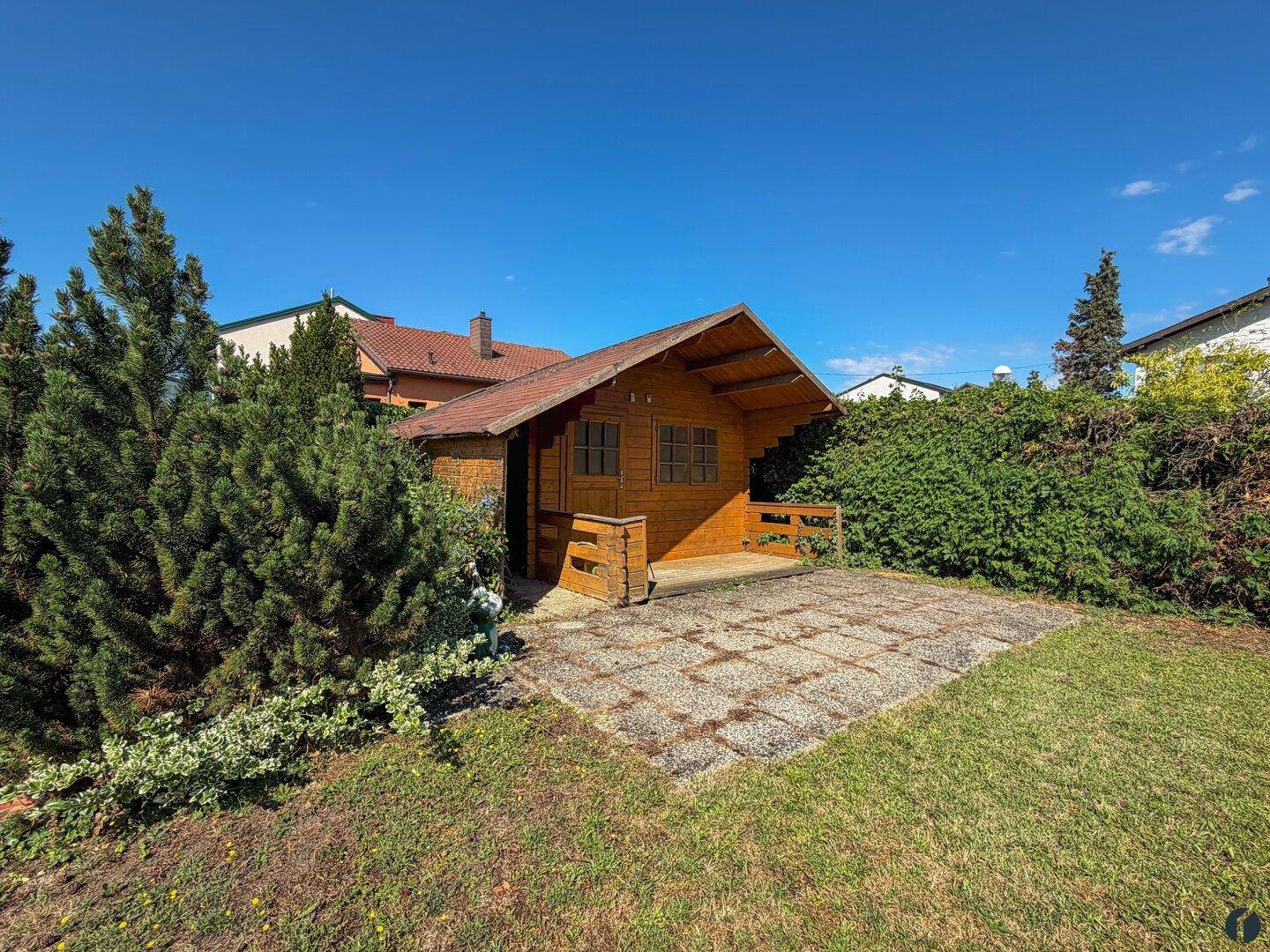 Garten mit einem kleinen Holzgartenhaus und einer gepflasterten Terrasse für Entspannung im Freien.