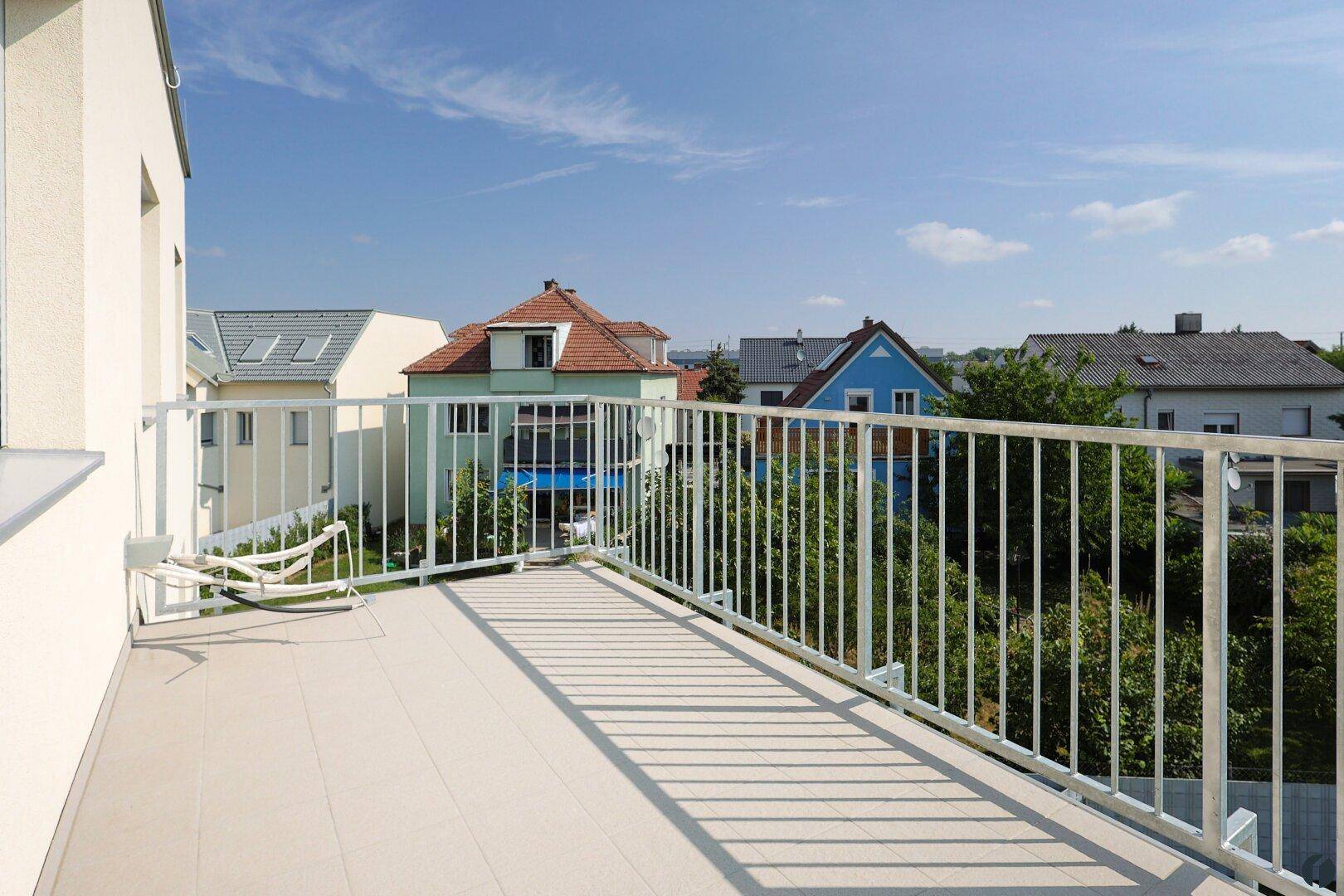 Geräumiger Balkon mit weißem Geländer und Blick auf die umliegenden Häuser und Gärten.