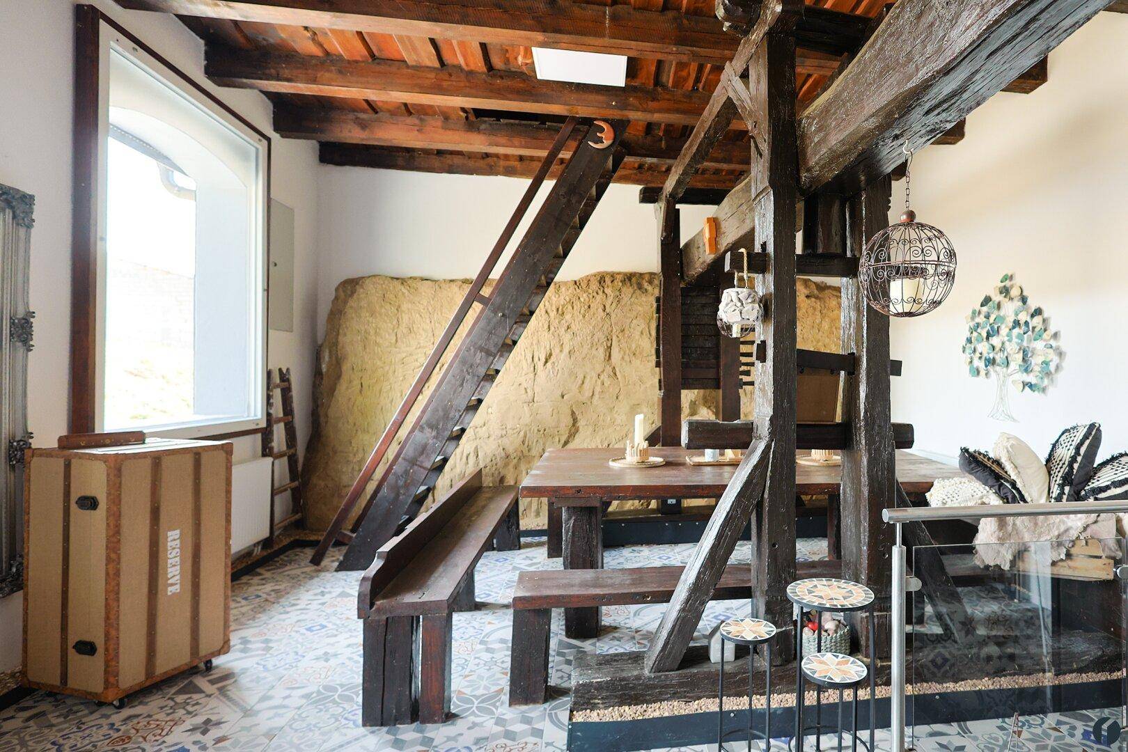 Heller Wohnbereich mit rustikalen Holzelementen, gemustertem Fliesenboden und großem Fenster.