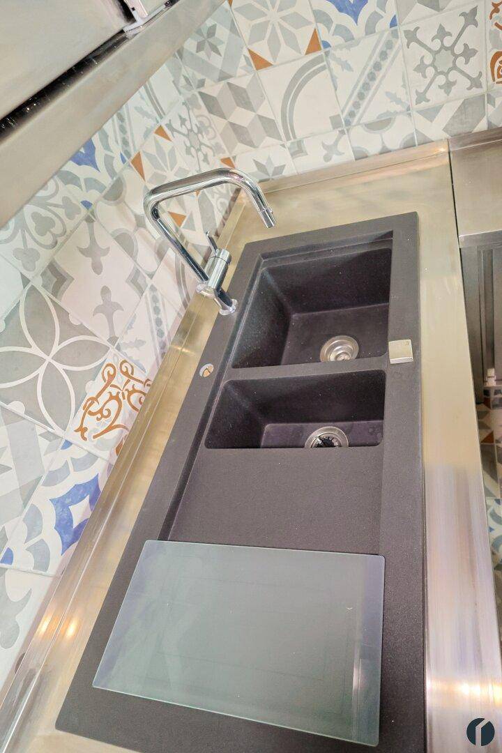 Nahaufnahme der Küchenspüle mit modernen Armaturen und farbenfrohen Fliesen als Spritzschutz.
