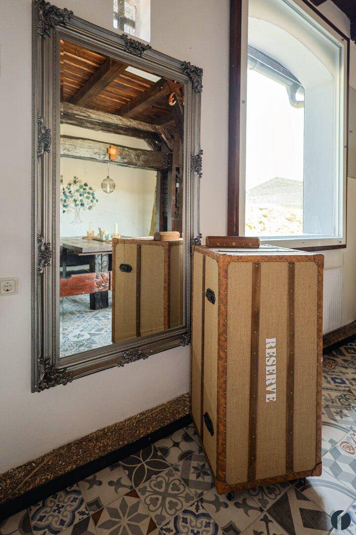 Großer verzierter Spiegel im Flur, der den rustikalen Innenraum und ein Fenster reflektiert.