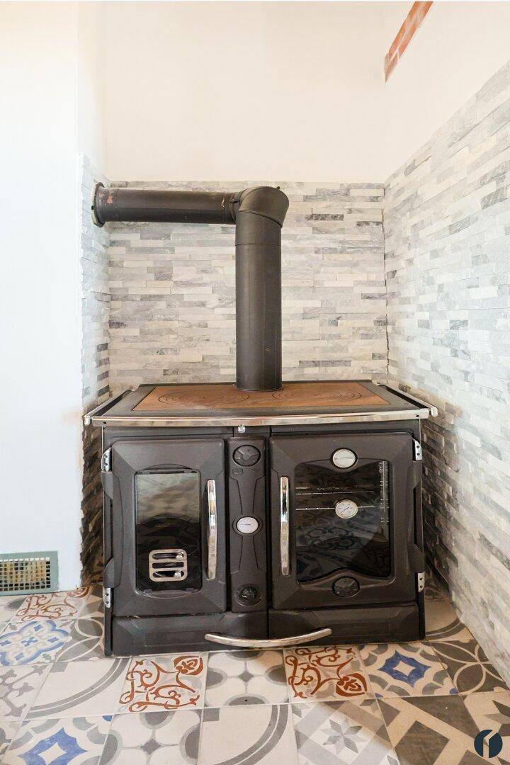 Traditioneller Holzofen mit Kochplatten und Backfach, umgeben von Steinwandfliesen.