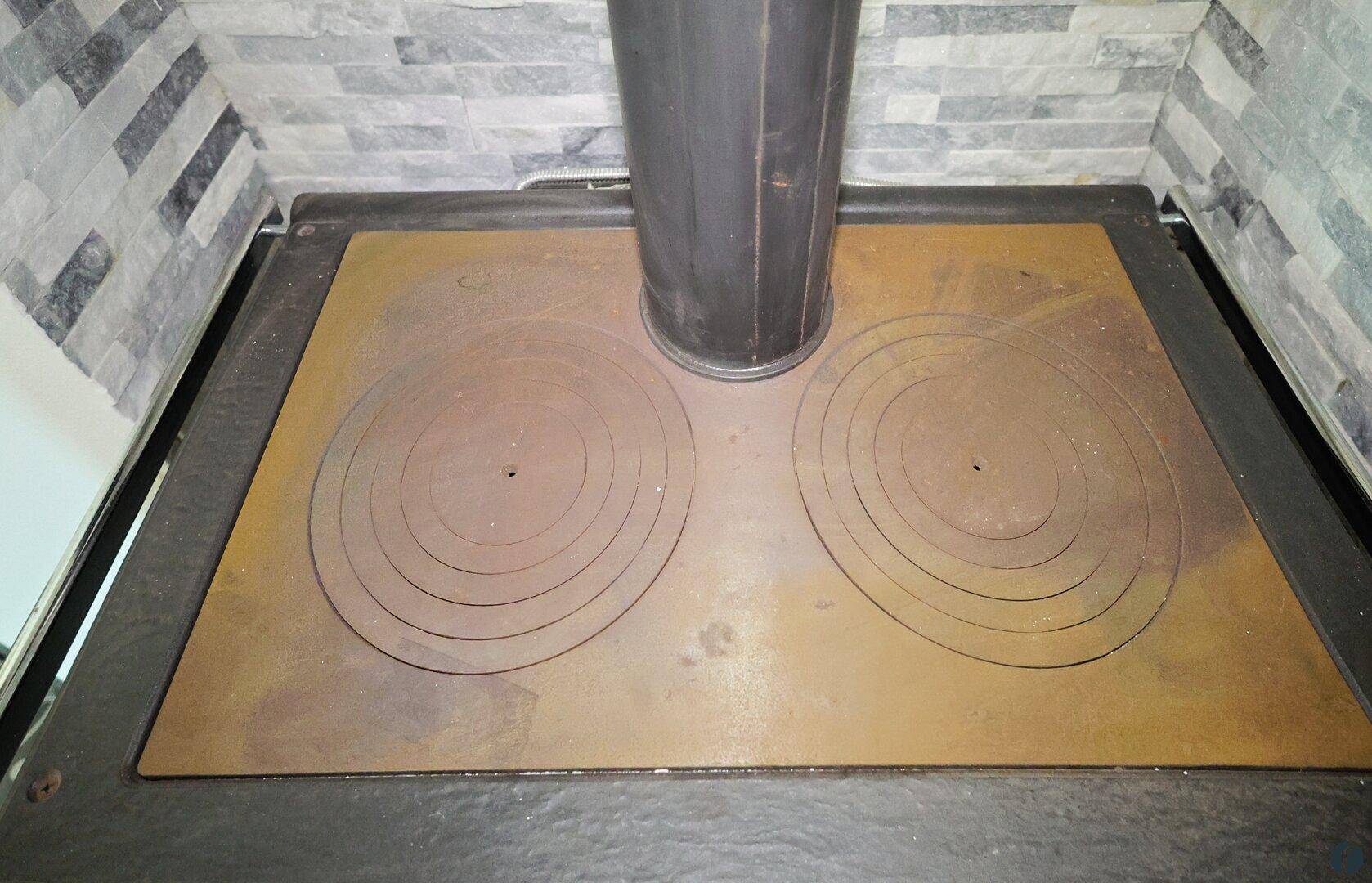 Detailansicht der Kochfläche des traditionellen Holzofens mit zwei runden Kochfeldern.