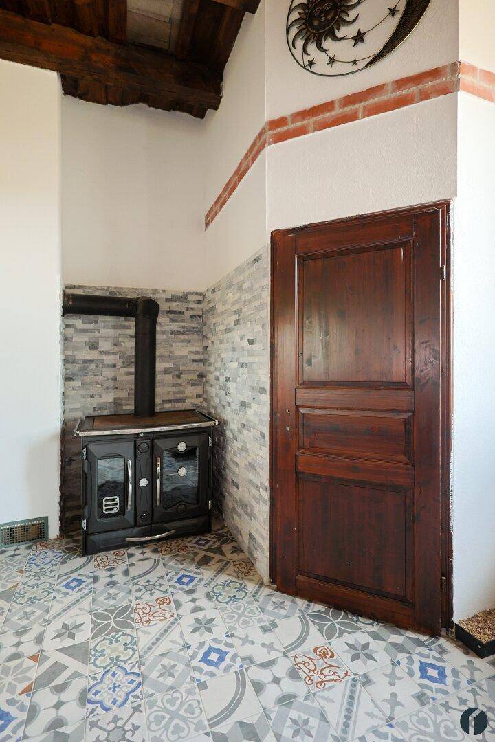Ecke der Küche mit traditionellem Holzofen, Steinwand und einer rustikalen Holztür.