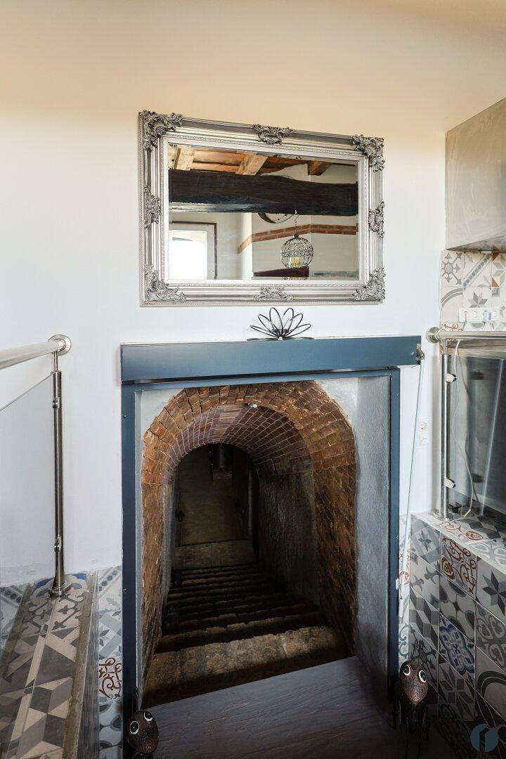 Eingang zum Weinkeller mit gemauertem Bogen und Treppe, umgeben von gemusterten Fliesen.