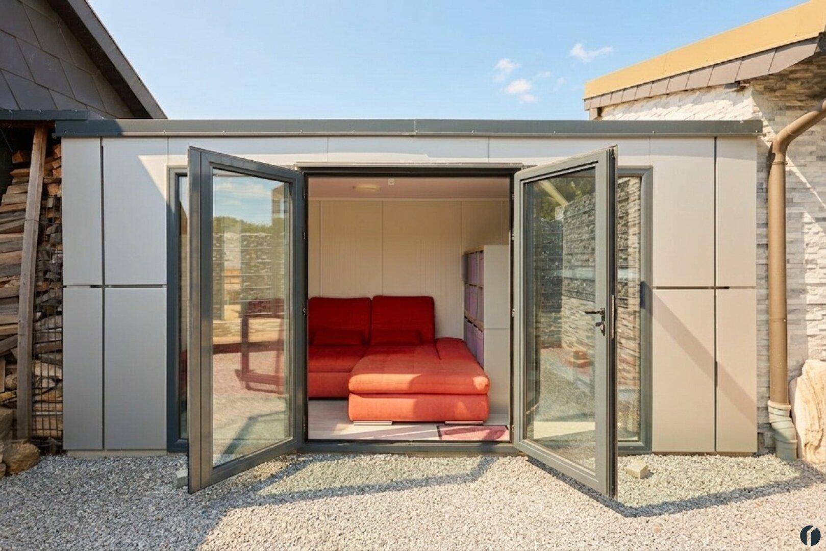 Kleines Nebengebäude mit geöffneten Falttüren, das einen gemütlichen Innenraum mit Sofa offenbart.