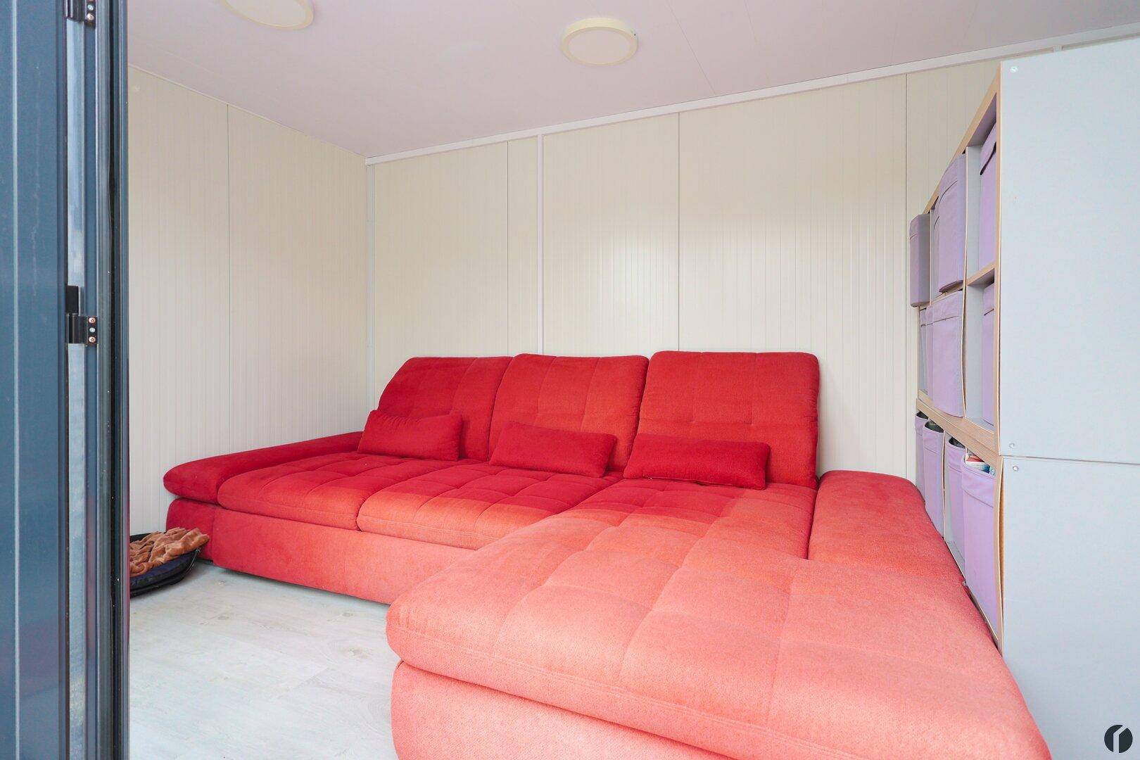 Gemütlicher Innenraum mit rotem Ecksofa und weißen Wandpaneelen, ideal als Rückzugsort.