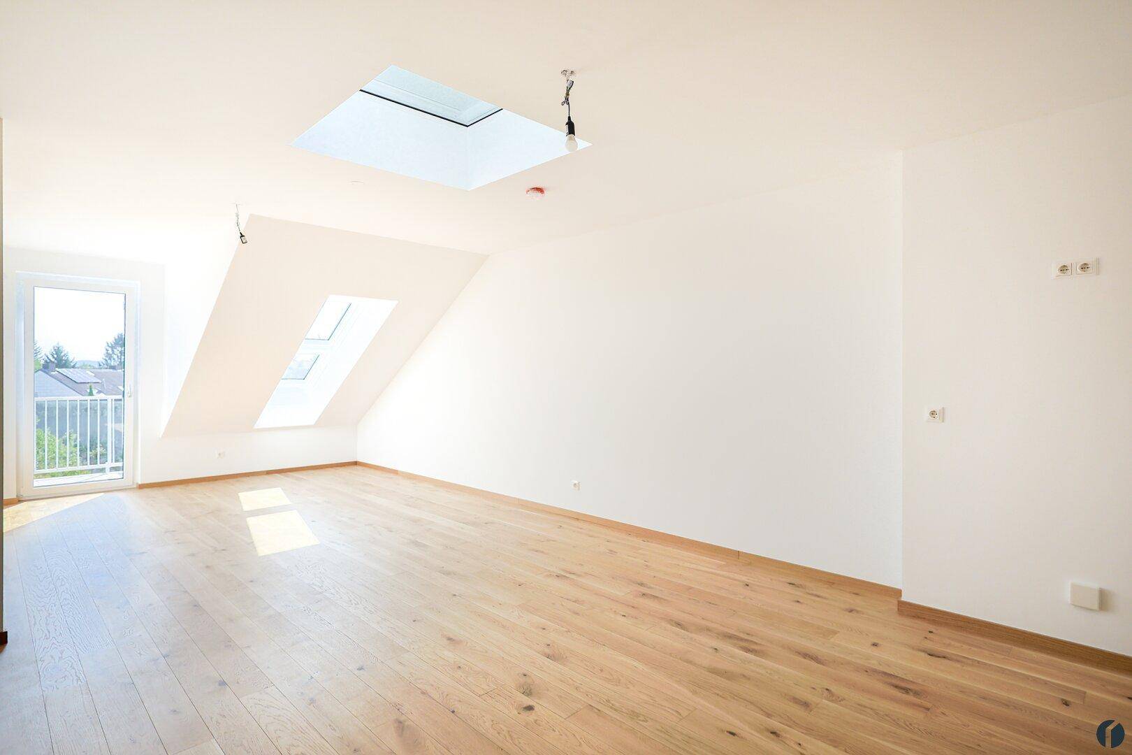 Lichtdurchfluteter Wohnraum mit Holzboden, Dachschrägen und Zugang zu einem französischen Balkon.