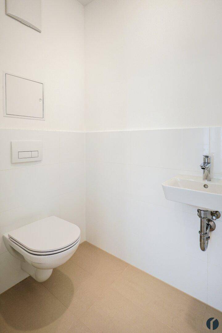 Separates WC mit wandhängender Toilette, kleinem Waschbecken und weißen Fliesen.
