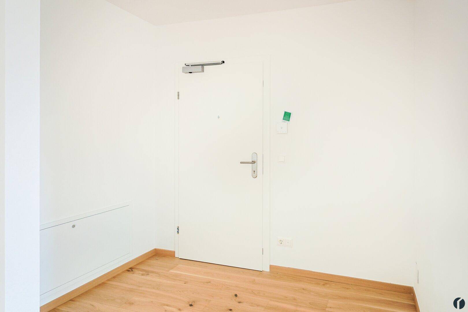 Eingangsbereich mit Holzboden und weißer Tür, die in die Wohnung führt.