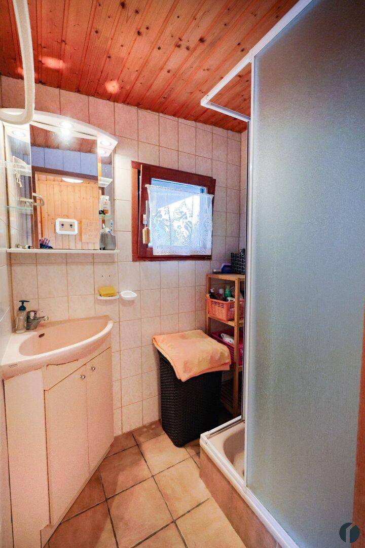 Badezimmer mit Fliesen, Duschkabine, Waschbecken und Holzdecke.
