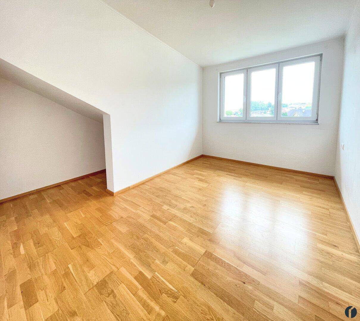 Helles Schlafzimmer mit Holzboden, Dachschräge und großen Fenstern für viel Tageslicht.