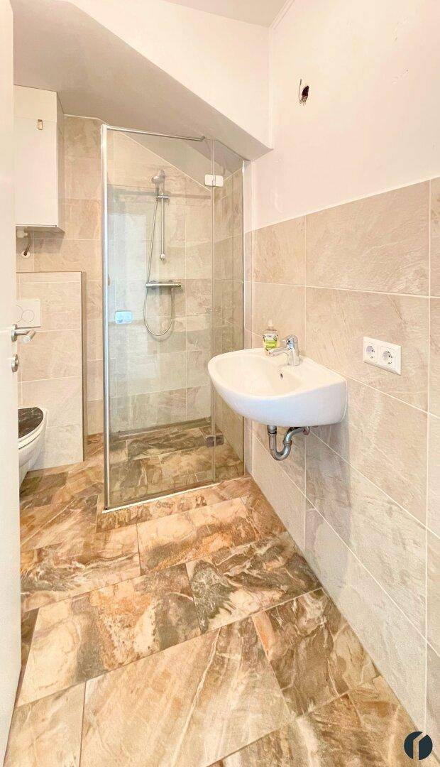 Modernes Badezimmer mit Fliesenboden, Duschkabine und wandhängendem WC in neutralen Farbtönen.