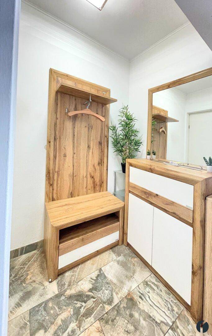 Heller Eingangsbereich mit Holzgarderobe, Spiegel und gemustertem Fliesenboden.