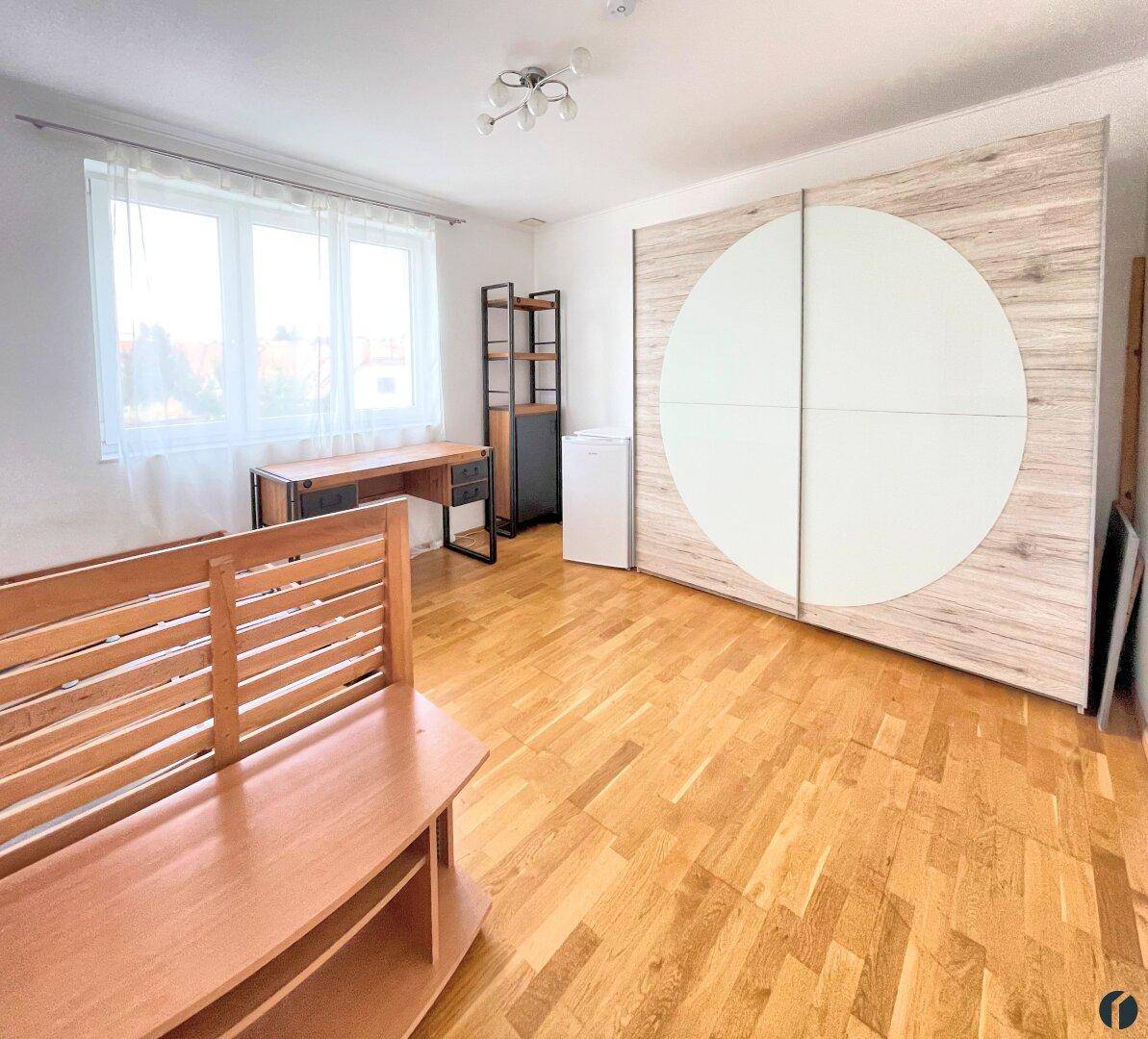Geräumiges Zimmer mit Holzboden, großem Fenster und modernem Schiebetürenschrank.