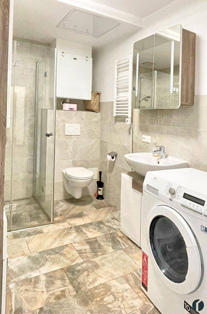 Modernes Badezimmer mit ebenerdiger Dusche, wandhängendem WC und Waschmaschine.