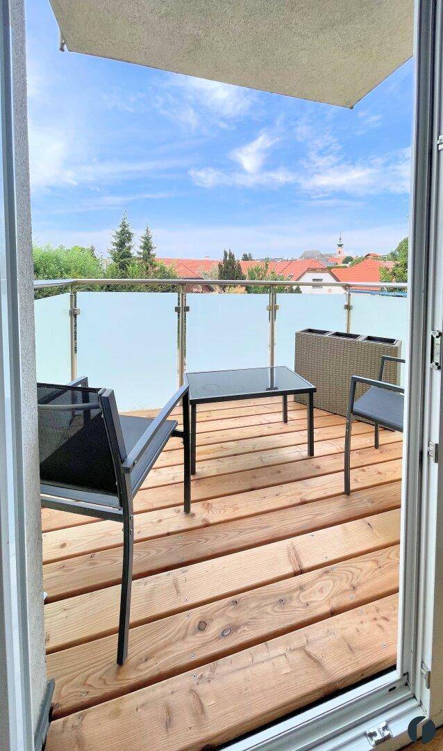 Balkon mit Holzboden, Glasgeländer und Blick auf die umliegende Bebauung.
