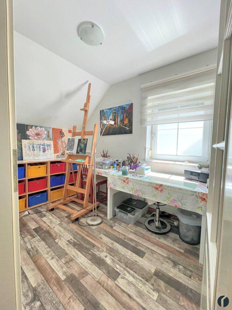 Helles Arbeitszimmer mit Schreibtisch, Kunstbedarf und Fenster unter einer Dachschräge.