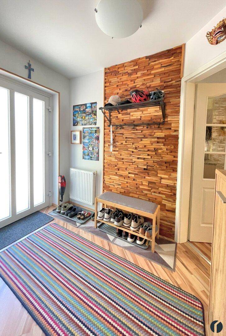 Einladender Flur mit Holzwandverkleidung, Schuhregal und farbenfrohem Teppich.