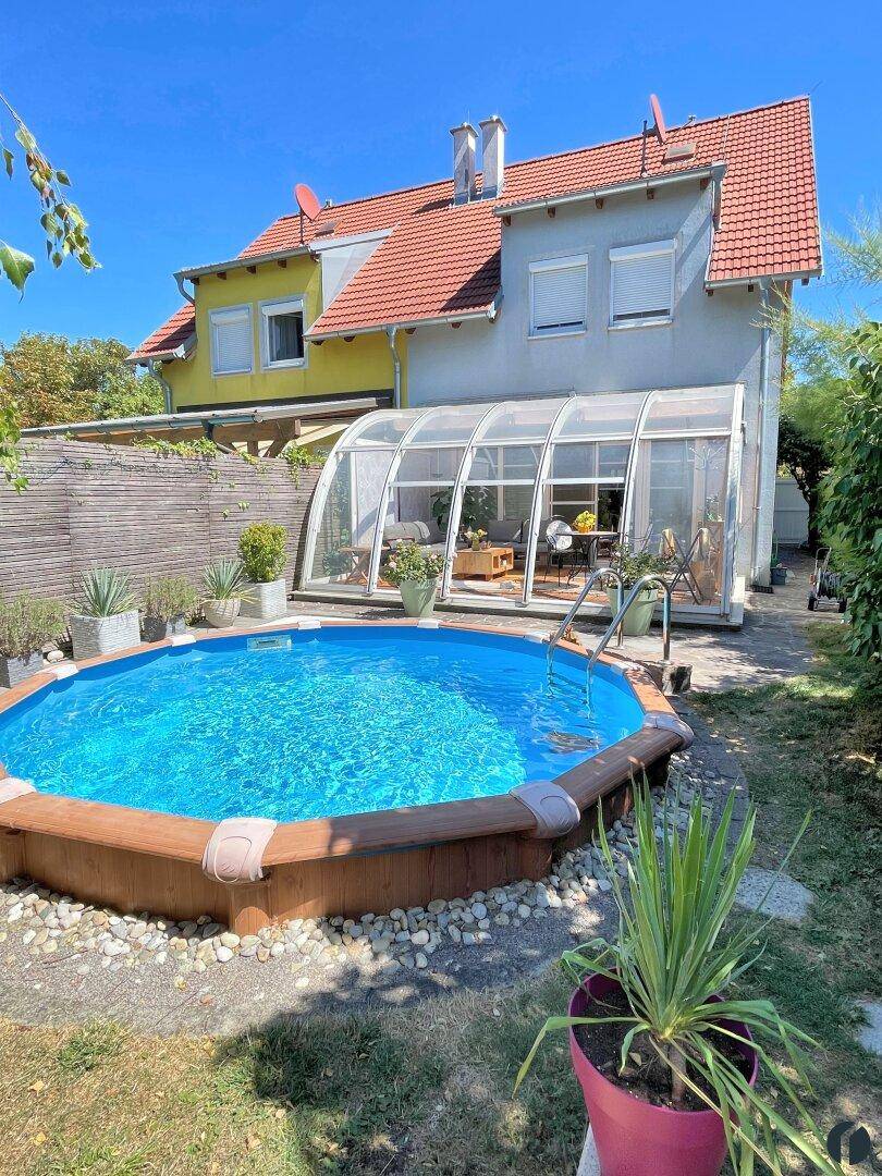 Hausfassade mit Garten, oberirdischem Pool und verglastem Wintergarten.