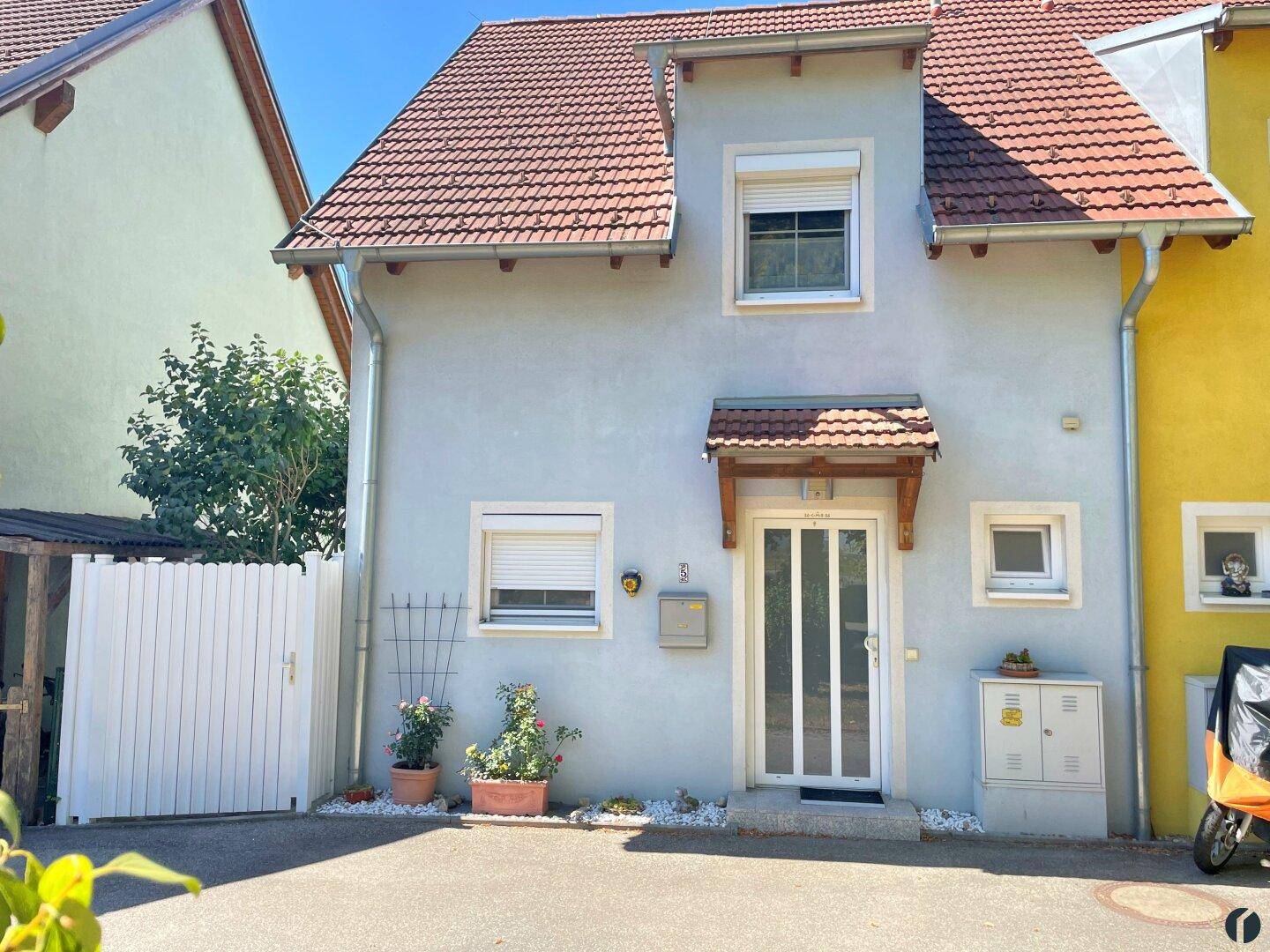 Vorderansicht des Hauses mit Eingangsbereich, kleinen Fenstern und gepflasterter Auffahrt.