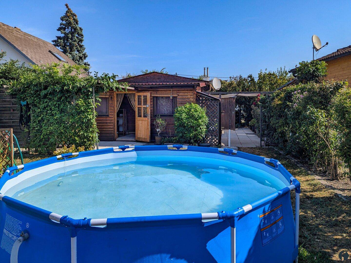 Aufstellbarer Pool im Gartenbereich vor dem charmanten Holzhaus an einem sonnigen Tag.