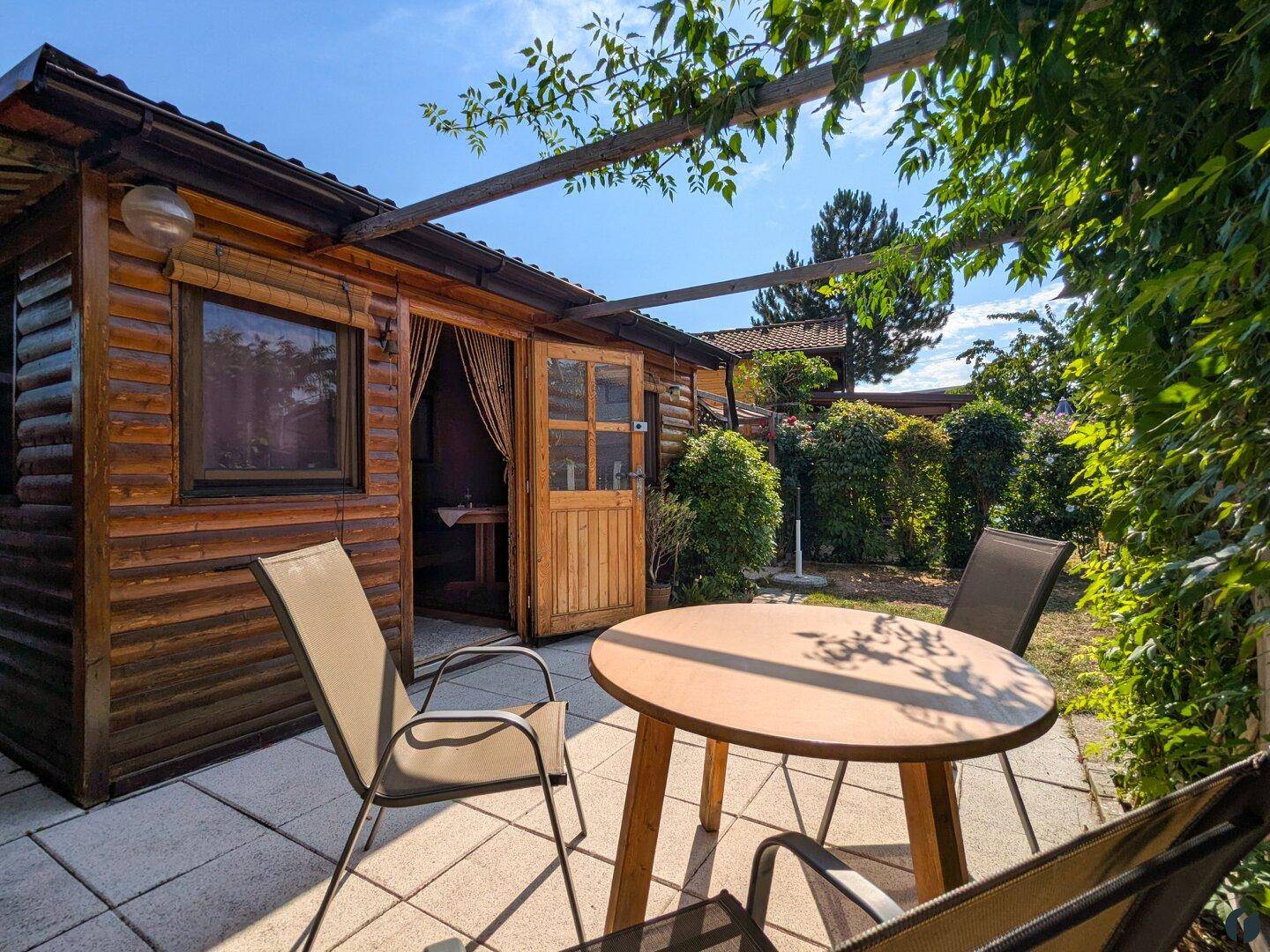 Gemütliche Terrasse mit Holztisch und Stühlen, direkt am Holzhaus mit Blick ins Grüne.