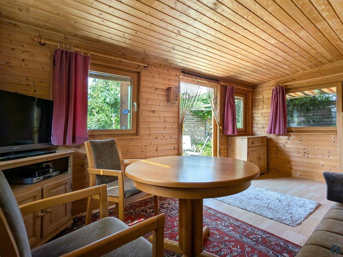 Helles Wohnzimmer im Holzhaus mit Holztisch, bequemen Stühlen und warmen Holztönen.