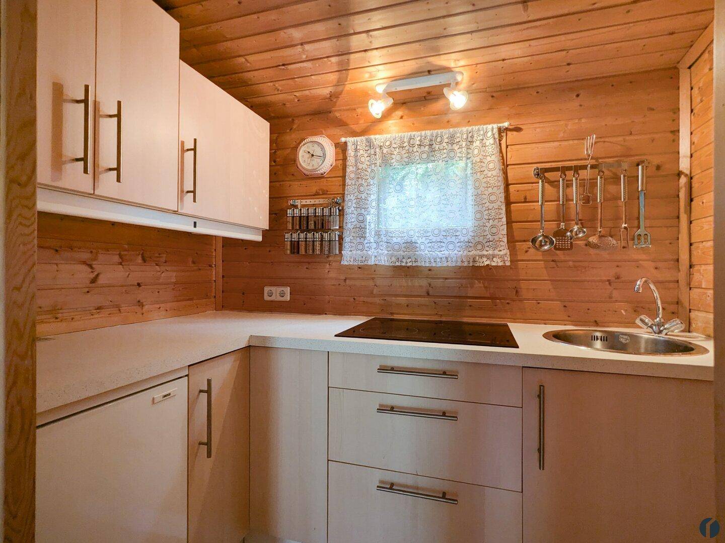 Kleine Küche im Holzhaus mit hellen Holzschränken, Spüle und Kochfeld.
