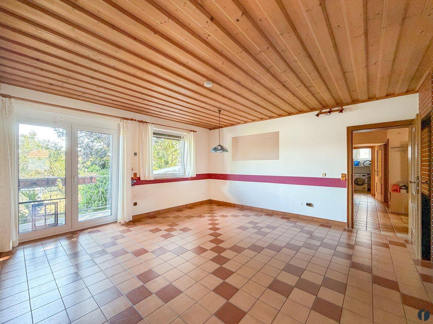 Geräumiges Wohnzimmer mit Fliesenboden, Holzdecke und Zugang zum Balkon.