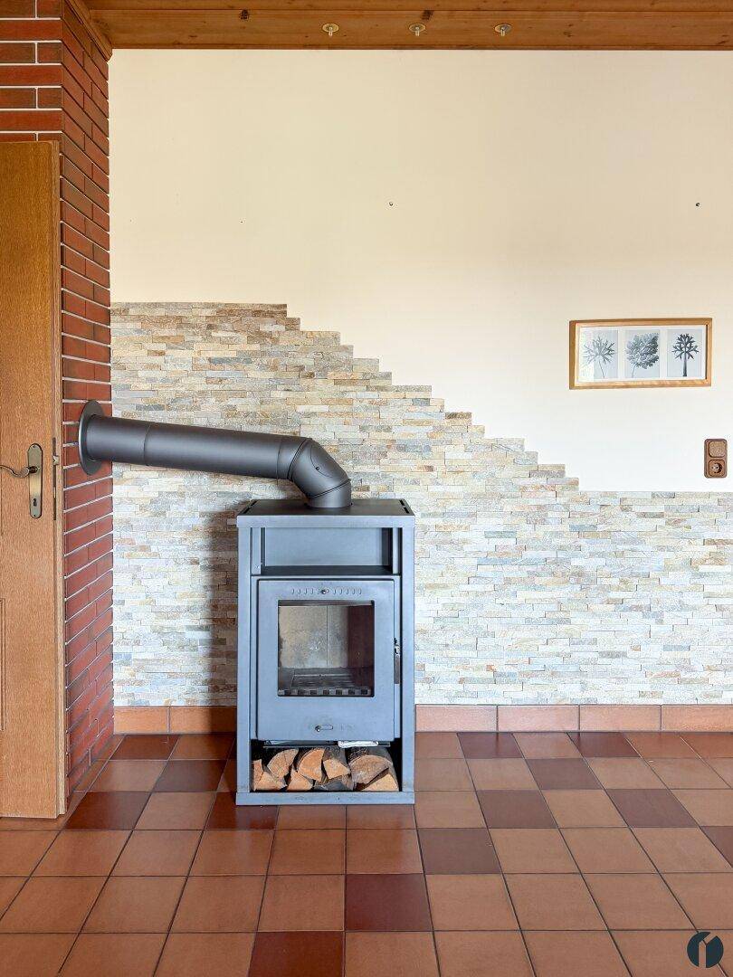 Detailansicht des modernen Kaminofens mit Holzscheiten und Steinwandverkleidung.