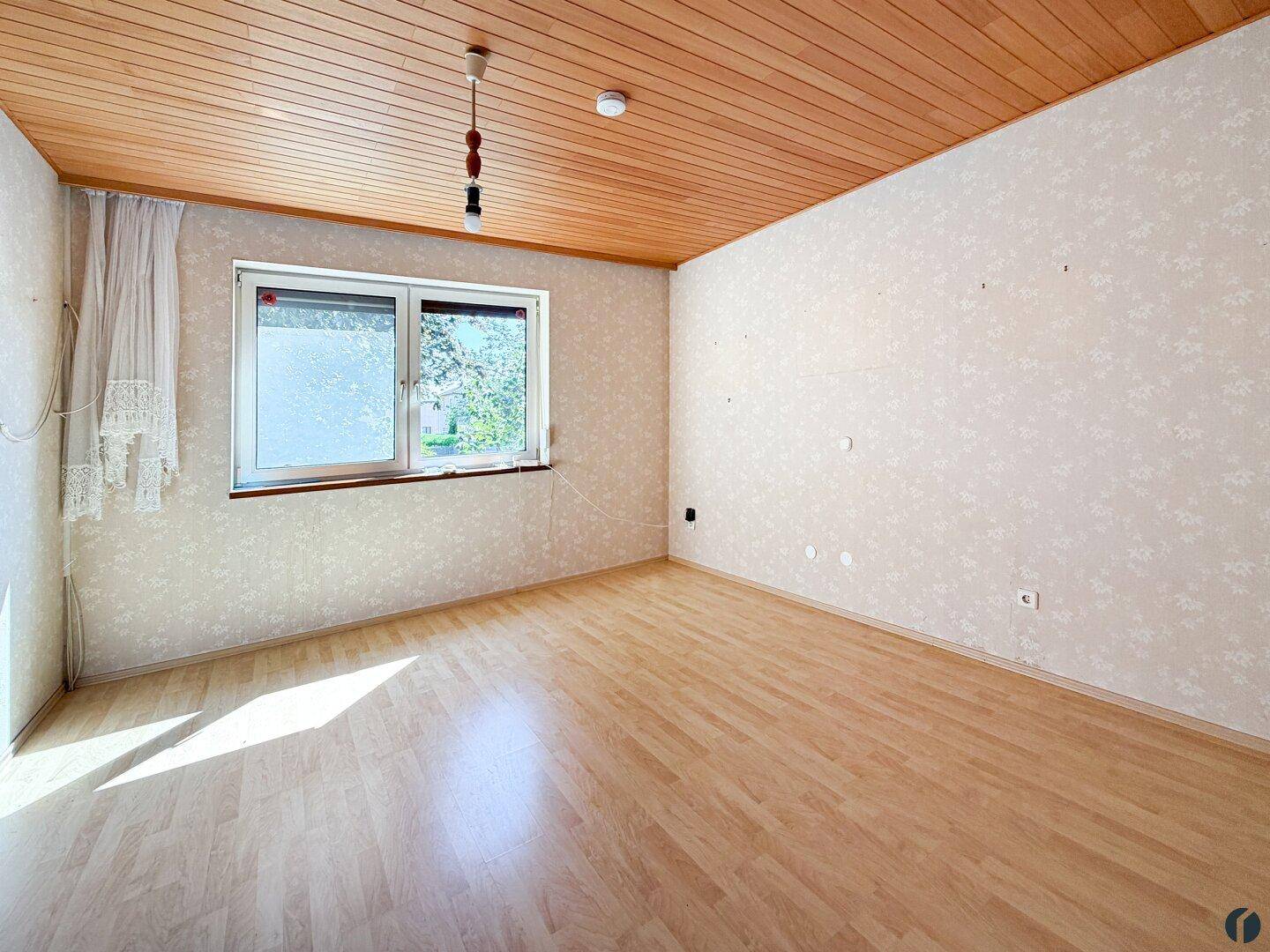 Geräumiges Schlafzimmer mit Laminatboden, Holzdecke und großem Fenster.