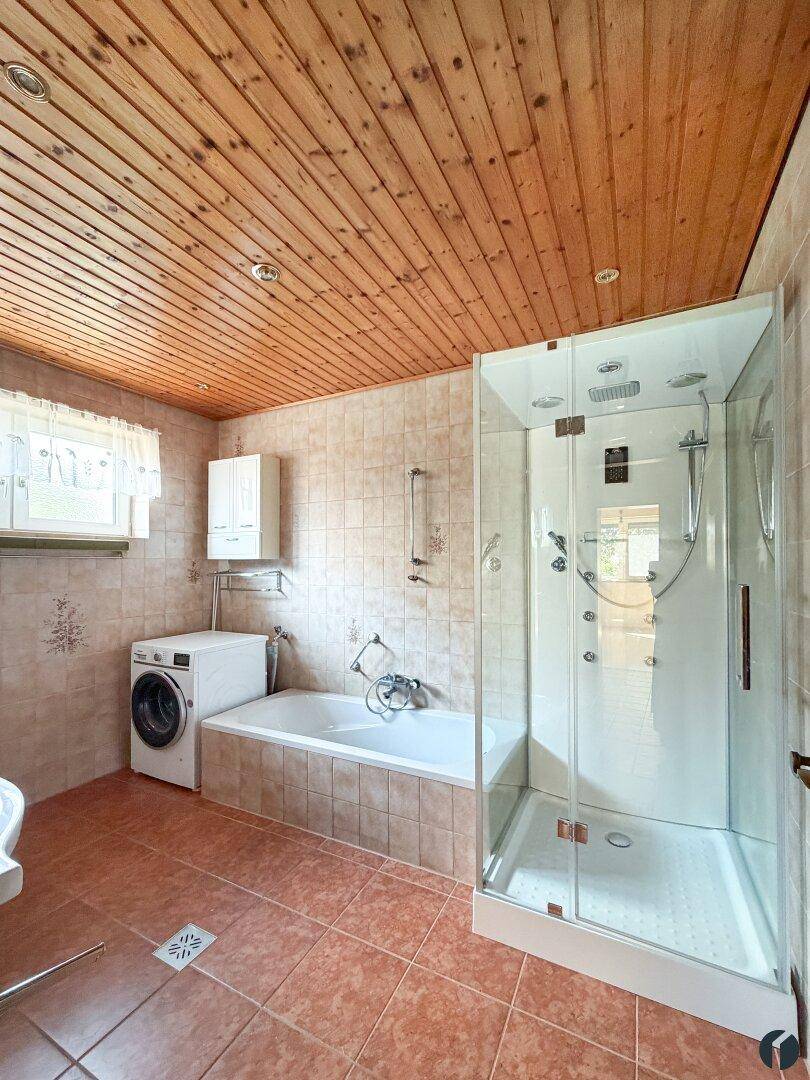 Badezimmer mit Duschkabine, Badewanne, Waschmaschine und Holzdecke.