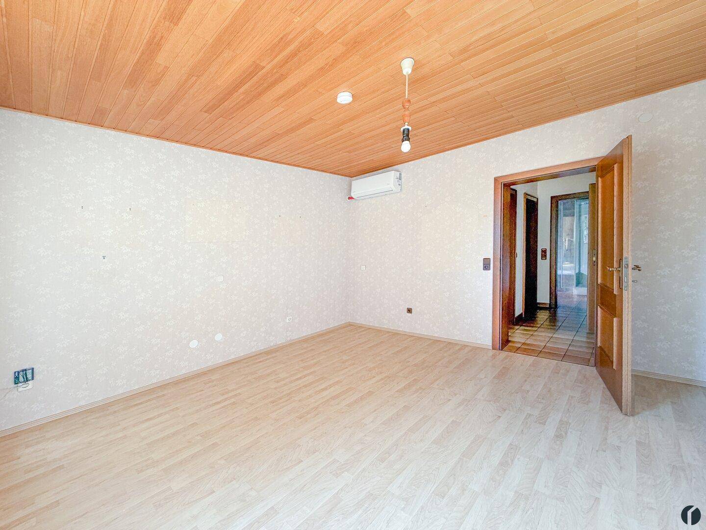 Helles Schlafzimmer mit Laminatboden, Holzdecke und Klimaanlage.